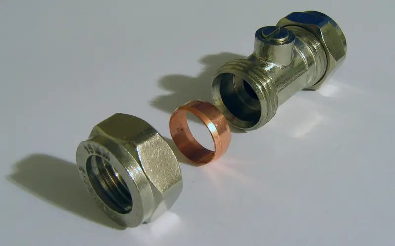 A 15 mm compression isolating valve with its nut and copper olive laid out beside it on a white surface
